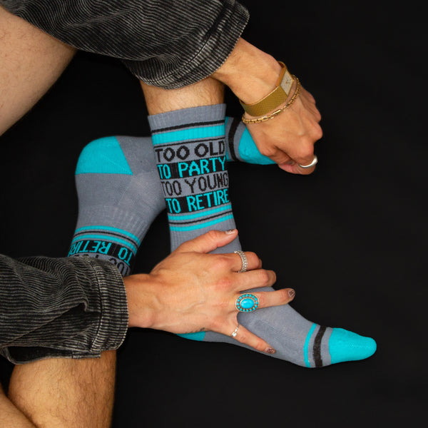 Lifestyle shot: Person wearing the 'Too Old To Party Too Young To Retire' socks. [lf]