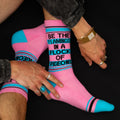 Lifestyle product shot: A person wearing the 'Be the flamingo' socks, hands visible, showcasing the sock detail against a dark background. [lf]