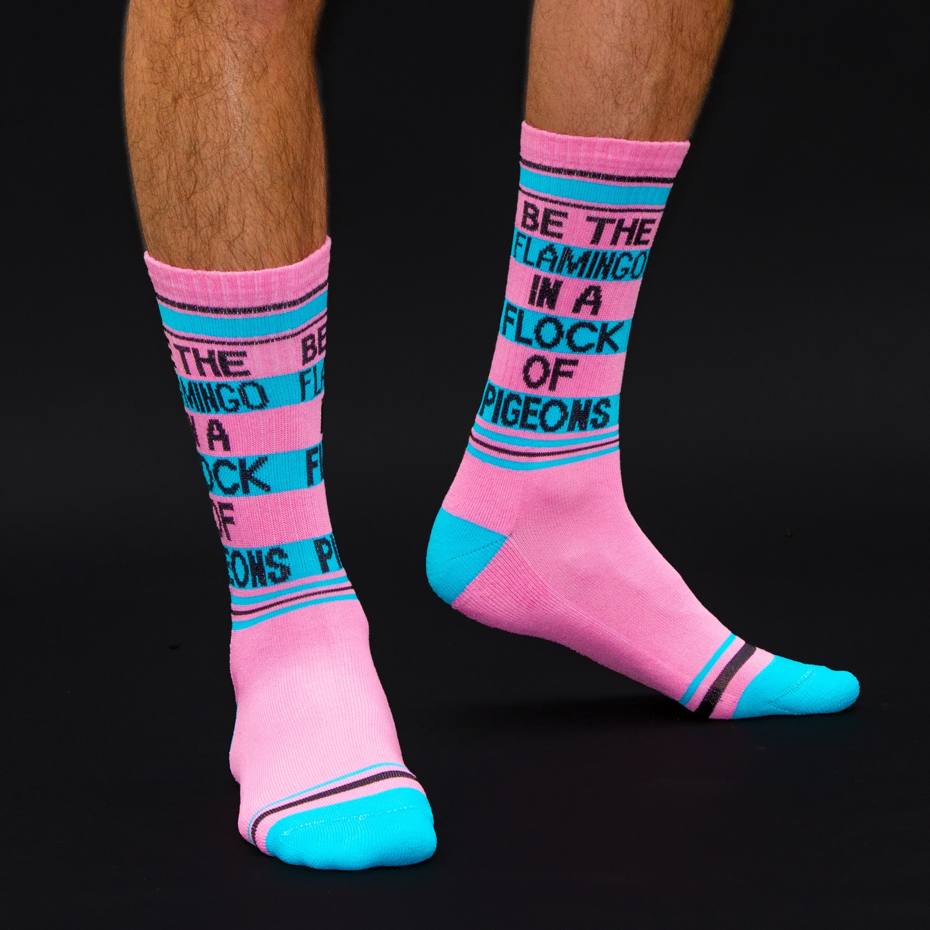 Studio shot: A pair of 'Be the flamingo' socks shown at an angle, showcasing the design and color against a black background. [lf]