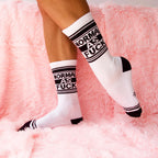 Lifestyle photo showcasing the 'Normal As Fuck' socks on a person's legs against a fluffy pink background. [lf]