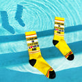 Lifestyle photo of yellow 'Someone in California Loves Me' socks resting on the edge of a pool. [lf]