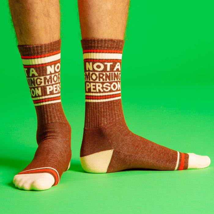 A pair of brown crew socks with white toes and heels and an orange stripe around the top. The left sock says 