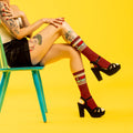 Lifestyle photo: Woman with tattoos wearing 'I Love Wine' socks and black platform heels against a yellow background.
