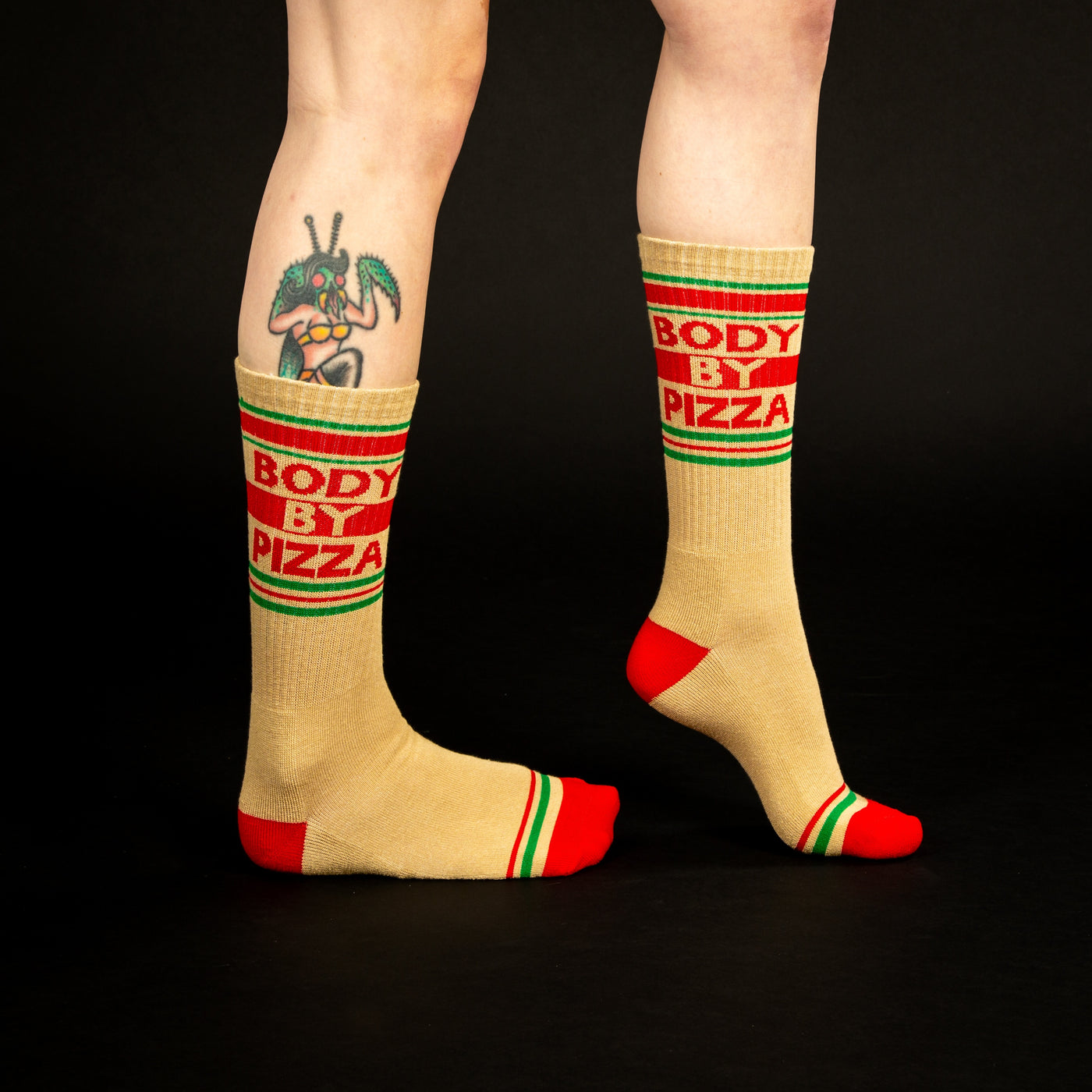 Lifestyle shot showing 'Body By Pizza' socks on a person's legs against a black background. [lf]