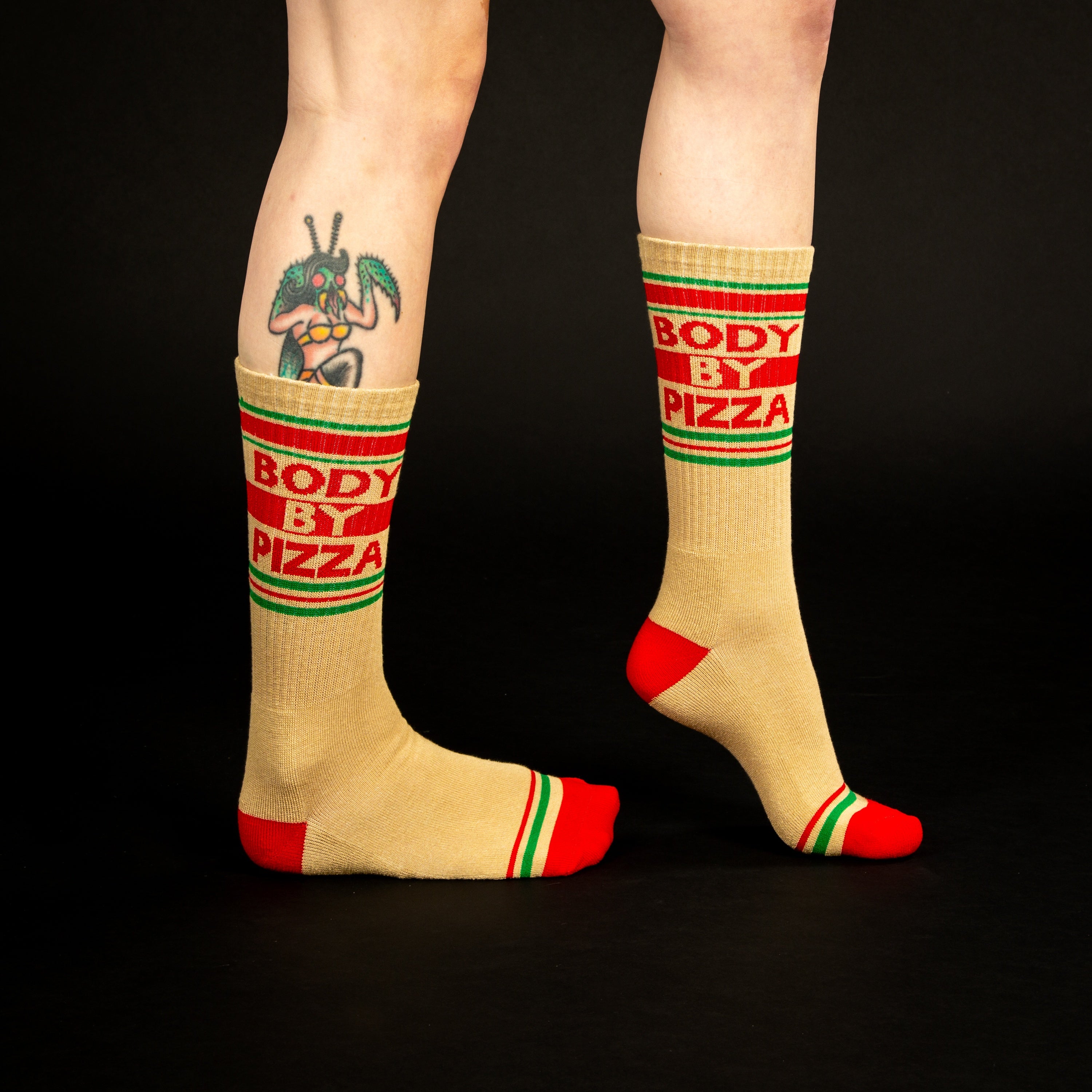 Lifestyle shot showing 'Body By Pizza' socks on a person's legs against a black background. [lf]