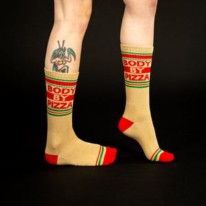 A pair of tan socks with red and green stripes at the top and red heels and toes. The socks say 