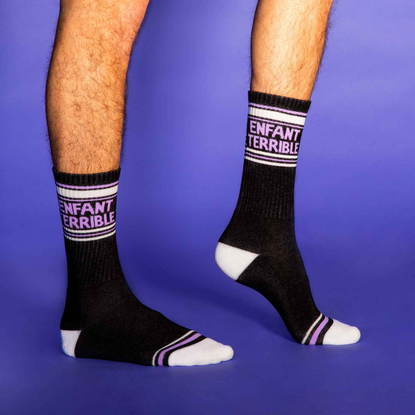 Lifestyle shot of a person wearing the Enfant Terrible socks against a purple background. [lf]