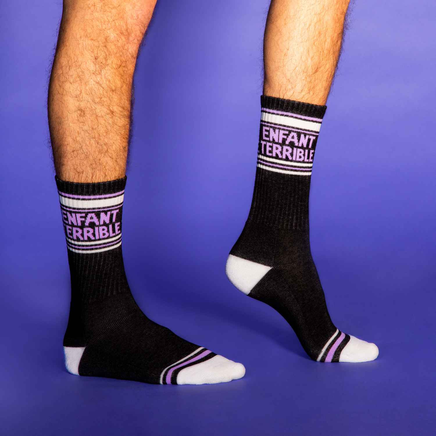 Lifestyle shot of a person wearing the Enfant Terrible socks against a purple background. [lf]