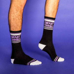 A person is modeling a pair of black socks with purple and white stripes at the top and purple text that reads 