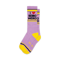 Pair of lavender crew socks with a yellow cuff and heel. The socks feature a graphic that reads 'I love being weird' in black text with a red heart.