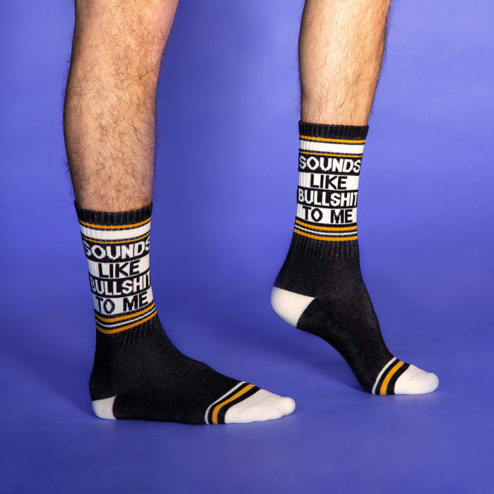 A pair of black socks with white and yellow stripes at the top and white toes and heels. The socks have the words 