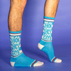 Lifestyle shot: A man's legs wearing the 'Real Men Admit They Love Cats' socks against a purple background. [lf]