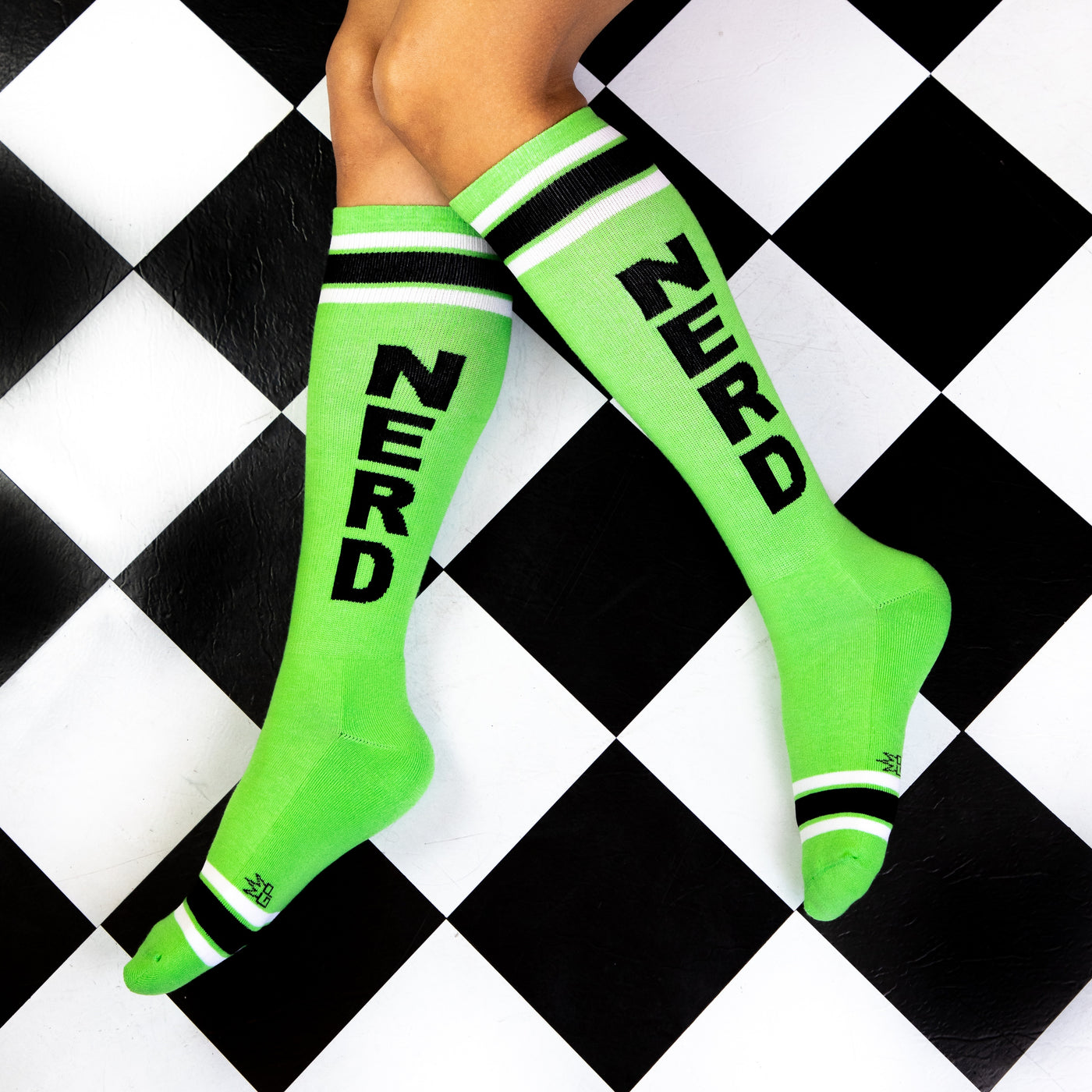 Lifestyle shot of a person wearing the lime green 'Nerd' socks on a black and white checkered floor. [lf]