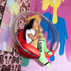 A woman with curly hair sits in a clear bubble chair, showing off her lime green 'Nerd' socks. [lf]