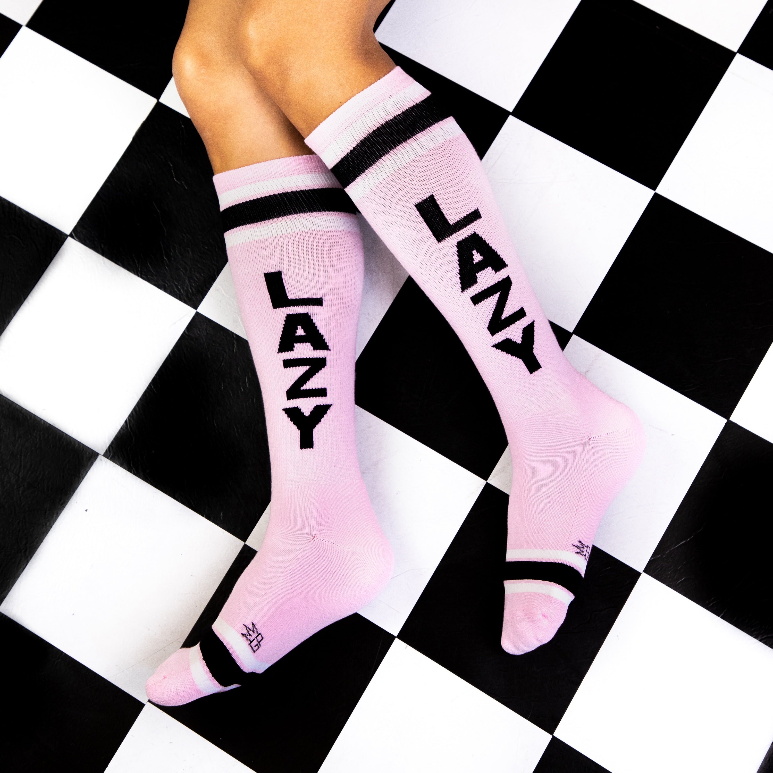 Lifestyle shot of 'Lazy' socks on a person's legs, showcasing the socks' fit and style on a black and white checkered floor. [lf]