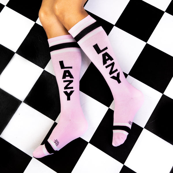 Lifestyle shot of 'Lazy' socks on a person's legs, showcasing the socks' fit and style on a black and white checkered floor. [lf]