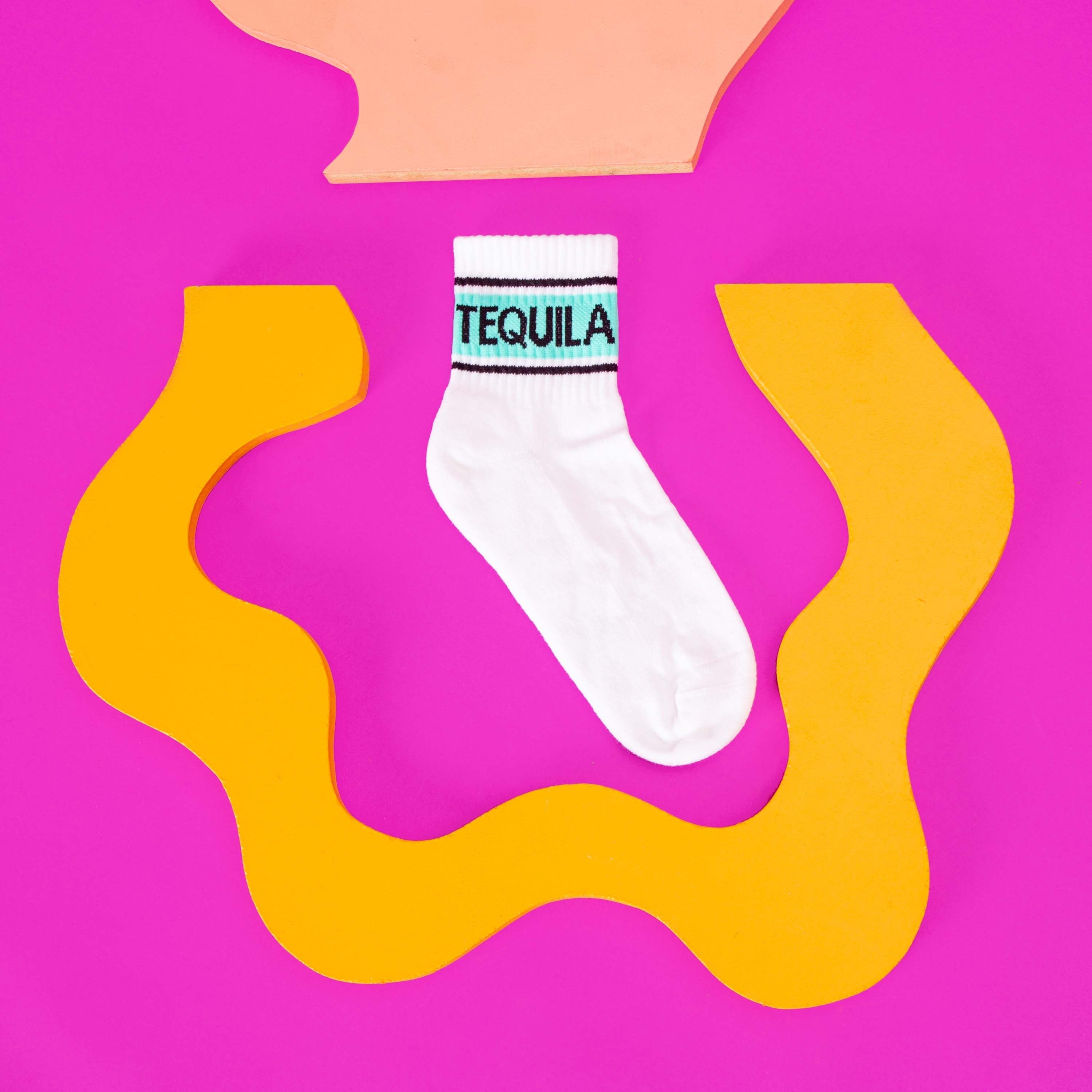 Flat lay product shot of a single Tequila sock on a vibrant pink background with yellow abstract shapes. [lf]