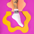Lifestyle shot of a person's foot wearing a white Snob sock against a colorful background. [lf]