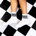 Flat lay showing a pair of white Snob socks on a black and white checkered floor. [lf]