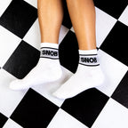 Flat lay showing a pair of white Snob socks on a black and white checkered floor. [lf]
