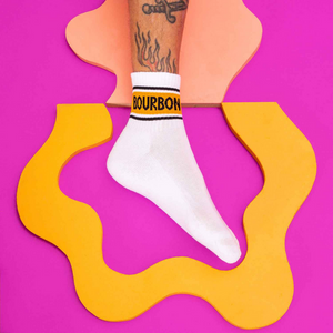 Lifestyle shot of a person's foot wearing one Bourbon sock on a vibrant pink and orange background.