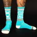 Lifestyle shot of a person wearing the teal 'I Do My Best Work In The Bathroom' crew socks.  The socks are shown on a dark background.