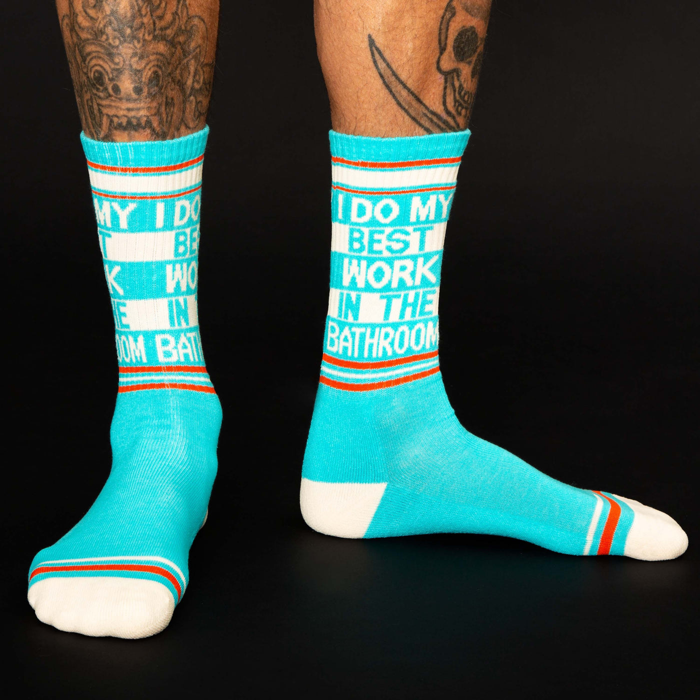 Lifestyle shot of a person wearing the teal 'I Do My Best Work In The Bathroom' crew socks.  The socks are shown on a dark background.