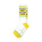 Pair of white crew socks with yellow and lime green stripes.  Text reads: 'Cocktails First Questions Later'.