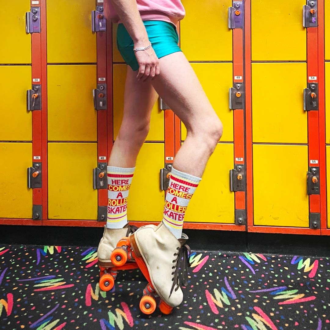 Lifestyle photo: Person wearing 'Here Comes A Roller Skater' socks while roller skating in a retro roller rink. [lf]