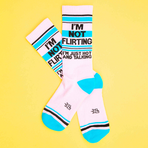 Flat lay of 'I'm Not Flirting' socks on a yellow background. The socks are pink, teal, and black.