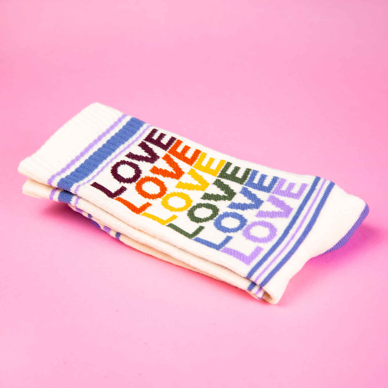 Folded pair of 'Love' rainbow socks on pink background. [lf]