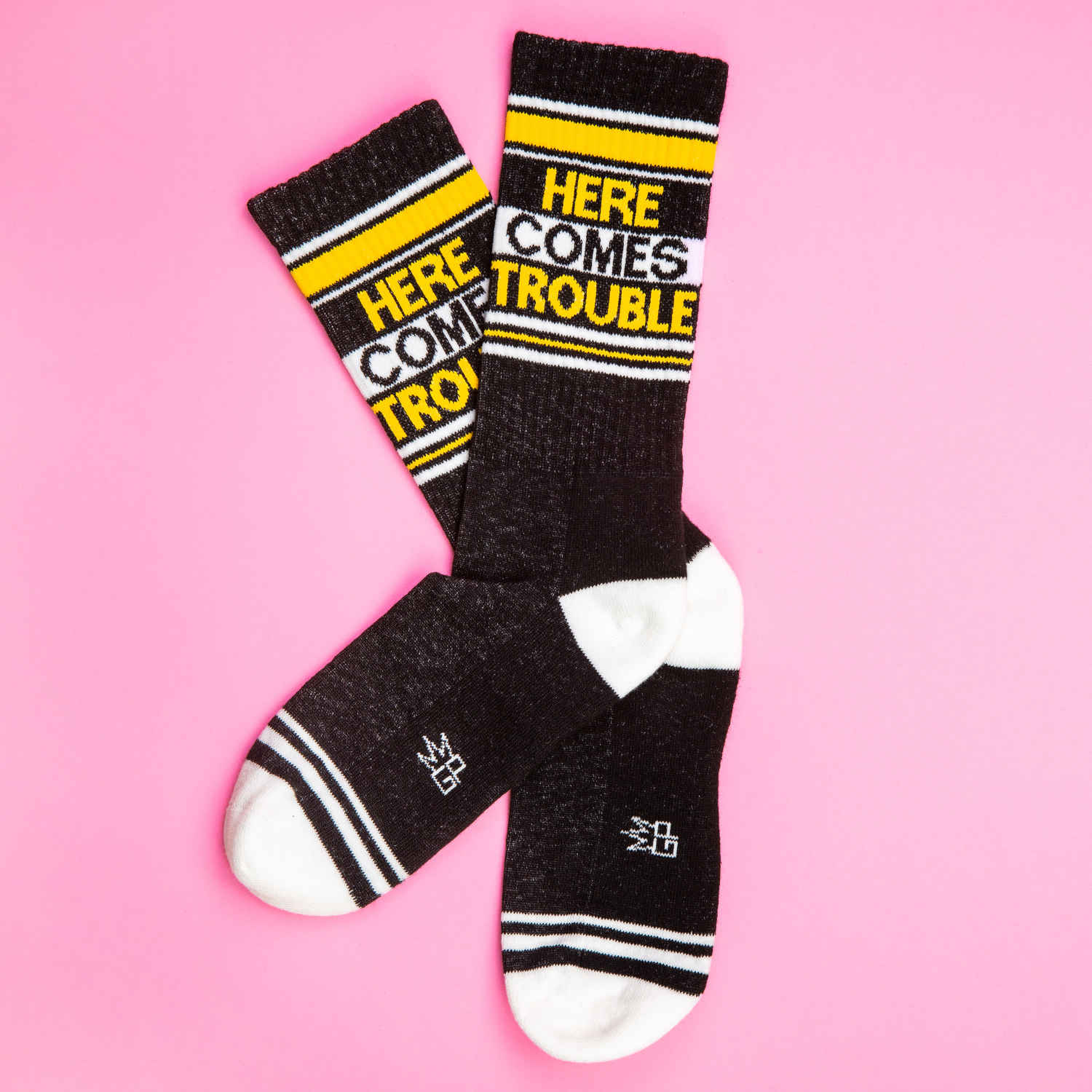 Flat lay of two 'Here Comes Trouble' socks on a pink background.