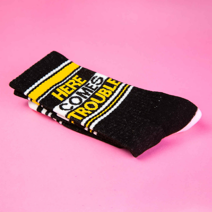 Close-up image of folded 'Here Comes Trouble' socks showcasing the design details on a pink background.