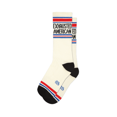 Pair of cream crew socks with 'Exhausted American' text in black, accented by red and blue stripes at the top and bottom.