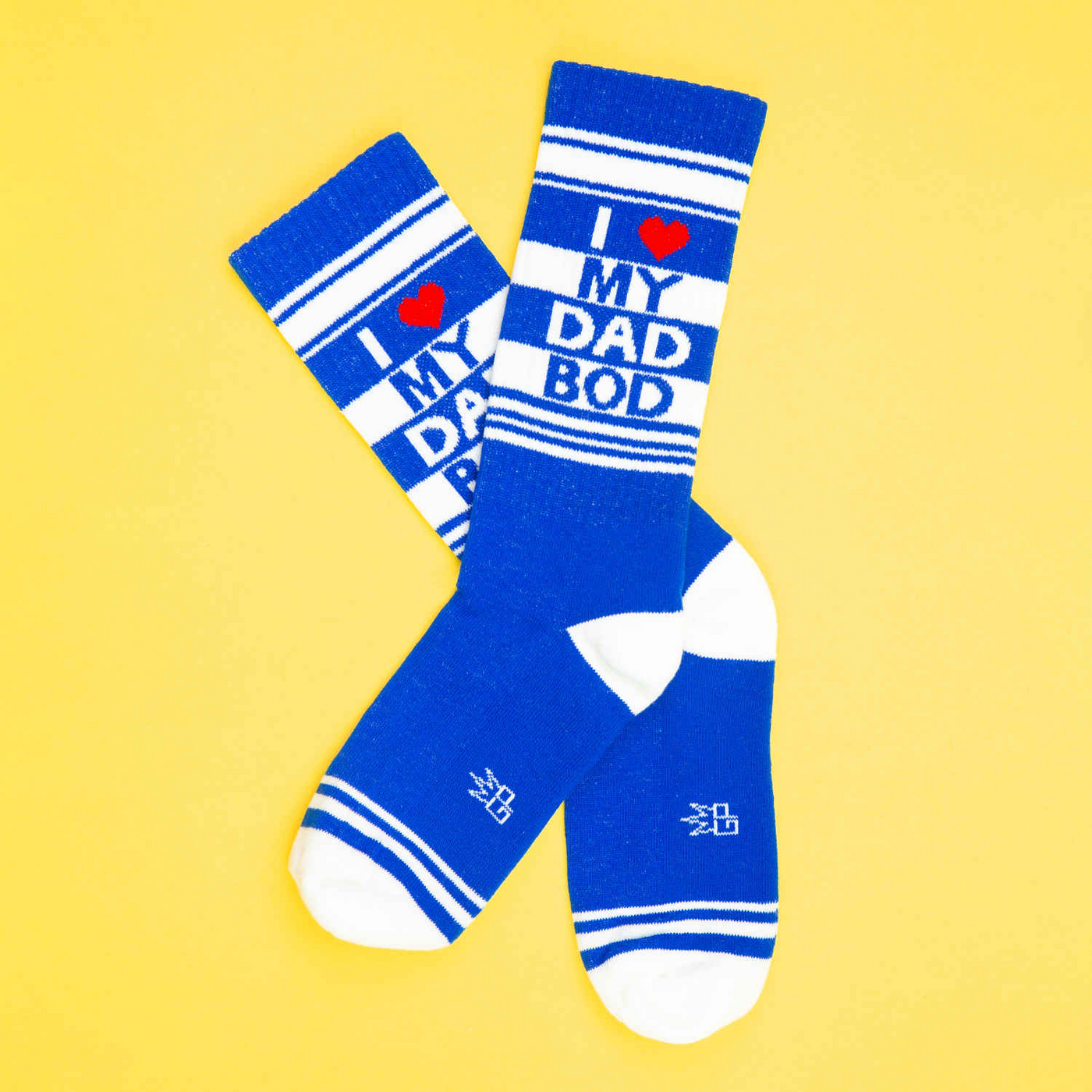 Flatlay of a pair of blue and white striped 'I love my dad bod' crew socks against a yellow background.