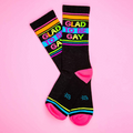 Flat lay of 'Glad To Be Gay' socks on a pink background.