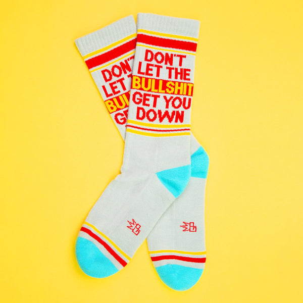 Flat lay of 'Don't Let The Bullshit Get You Down' socks against a yellow background. [lf]