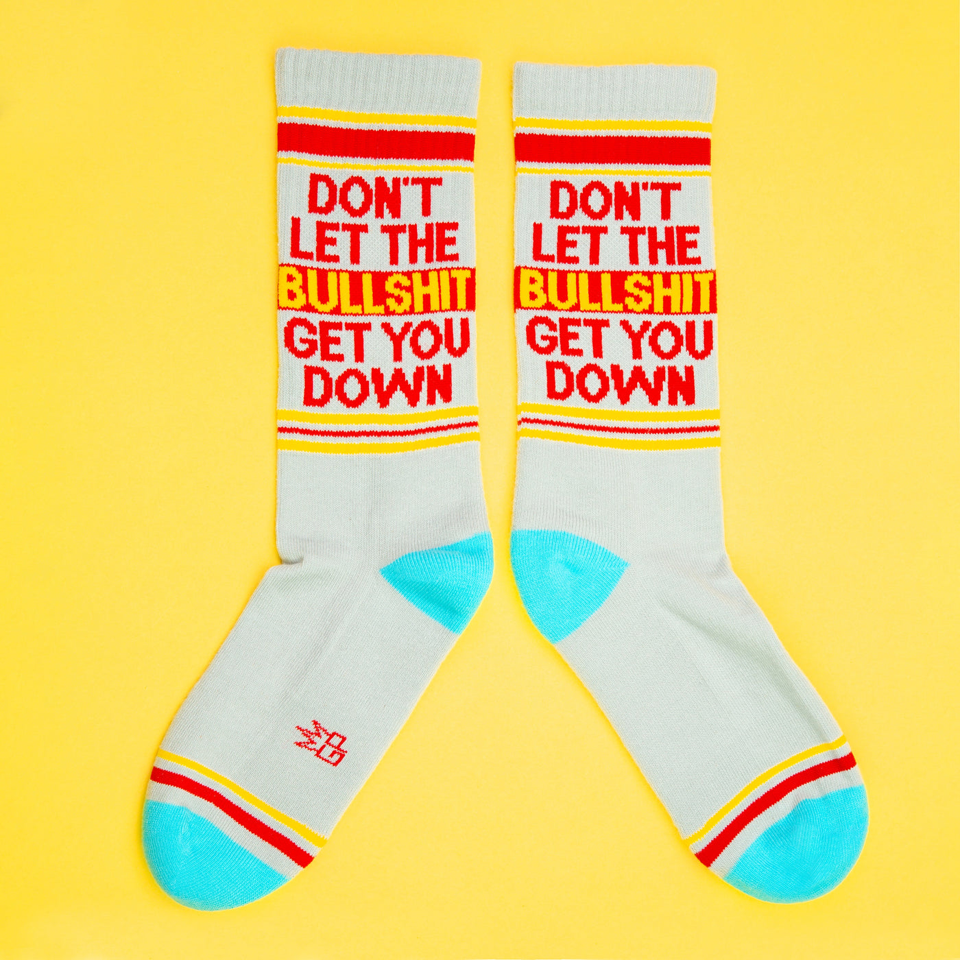 Two 'Don't Let The Bullshit Get You Down' socks laid flat on a yellow background, showcasing both sides of the design. [lf]