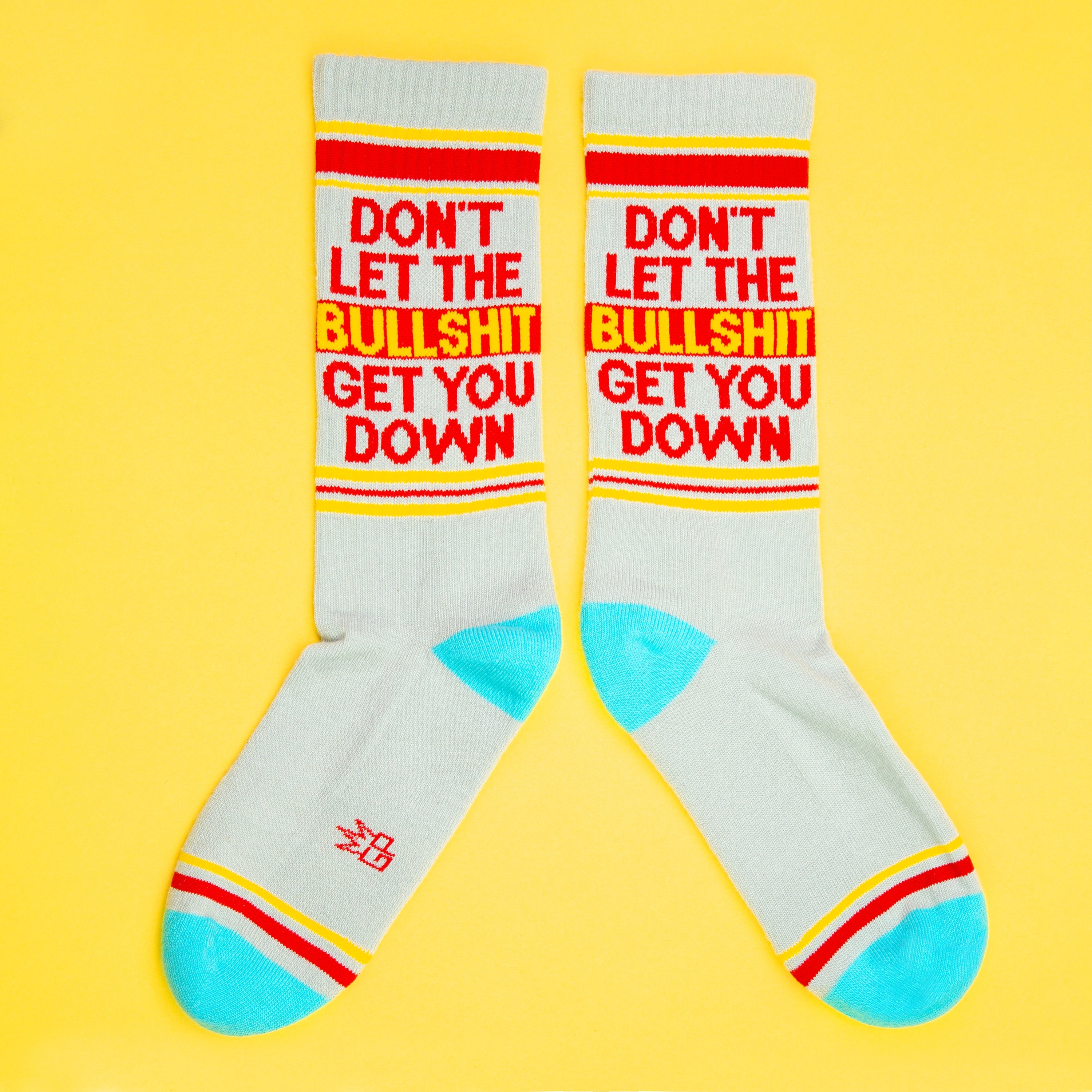 Two 'Don't Let The Bullshit Get You Down' socks laid flat on a yellow background, showcasing both sides of the design. [lf]
