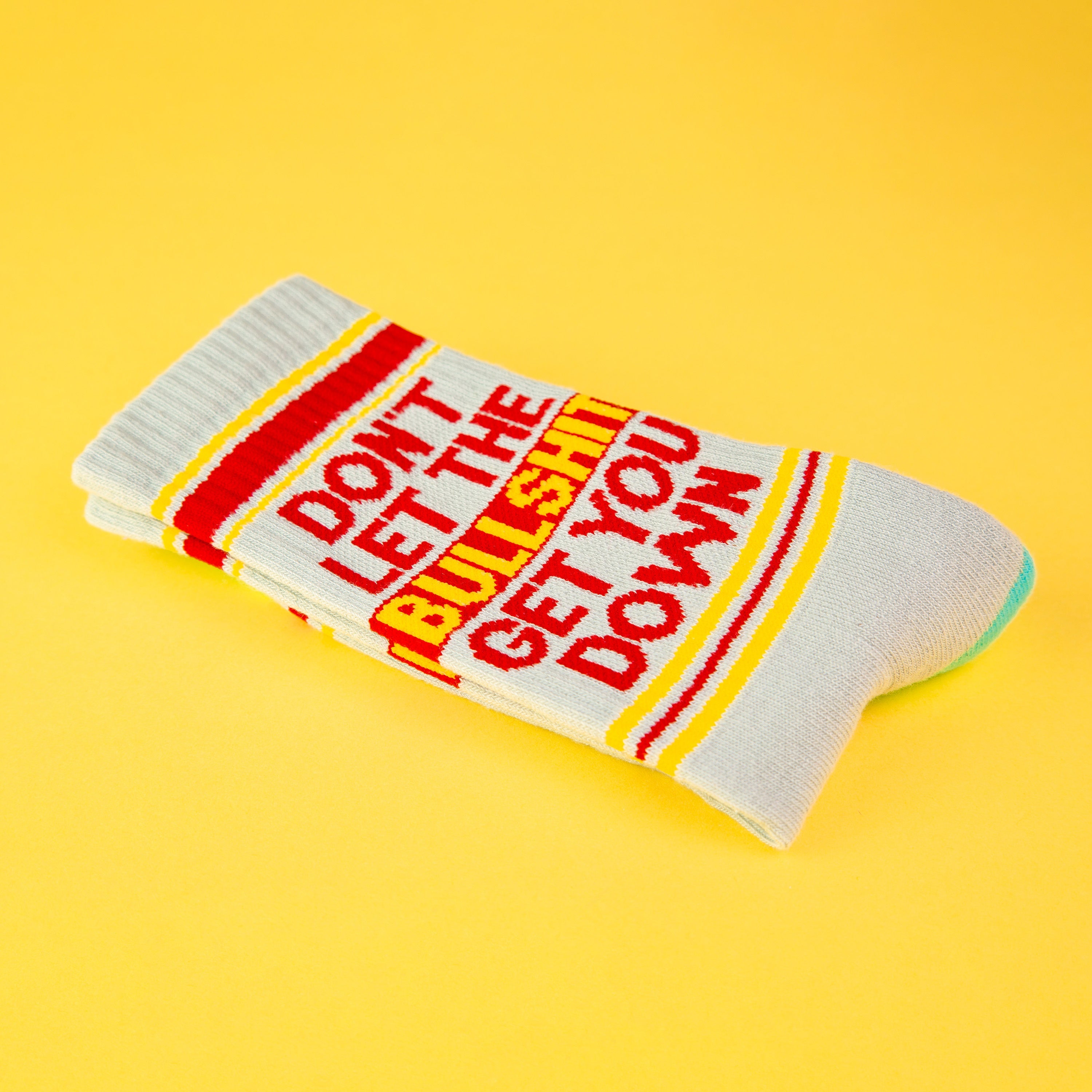 Close-up of a single 'Don't Let The Bullshit Get You Down' sock folded on a yellow background, highlighting the design details. [lf]