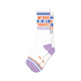 socks that are white with purple toes, heels, and cuffs. they have orange stripes above the cuffs and below the toes. the words 'my dog is my therapist' are written in capital letters on the front of the socks.