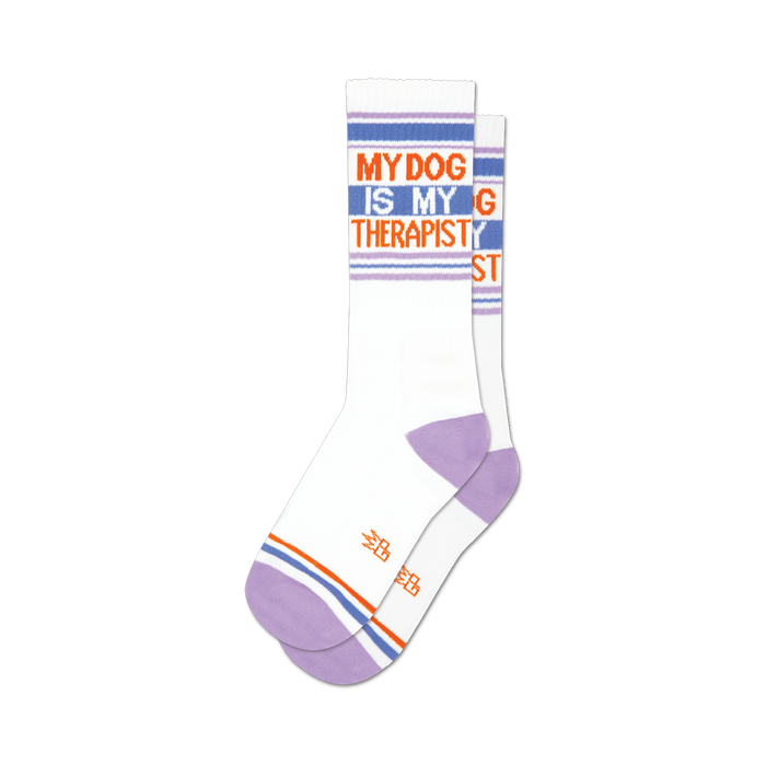 socks that are white with purple toes, heels, and cuffs. they have orange stripes above the cuffs and below the toes. the words 'my dog is my therapist' are written in capital letters on the front of the socks. }}