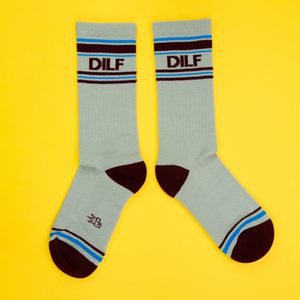 Flatlay product shot of a pair of light-grey DILF socks on a yellow background.  The socks feature maroon and light blue stripes.
