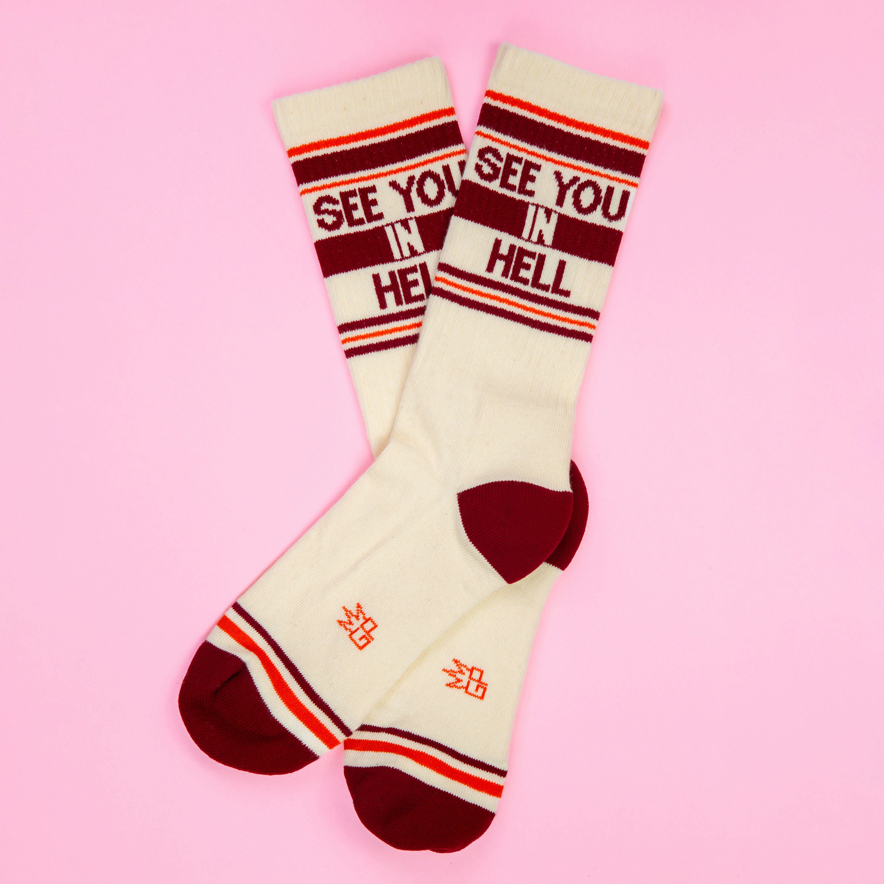 Flat lay of 'See You In Hell' socks on a pink background. [lf]