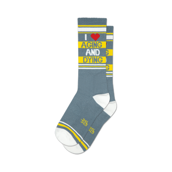 a pair of gray socks with white toes, heels, and cuffs. the socks have red and yellow stripes near the top and yellow stripes above the heel. the words 'i heart aging and dying' are written vertically on the front of the socks in red and yellow letters.