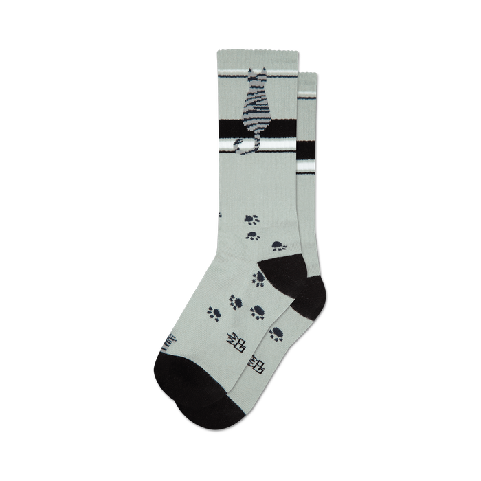 socks that are gray with a pattern of black cat paw prints. there is a black heel and toe with a gray toe seam. the top of the foot has a black band with two white stripes. the leg of the sock has a black cat sitting with its tail wrapped around its paws. the cat is gray with black stripes. }}