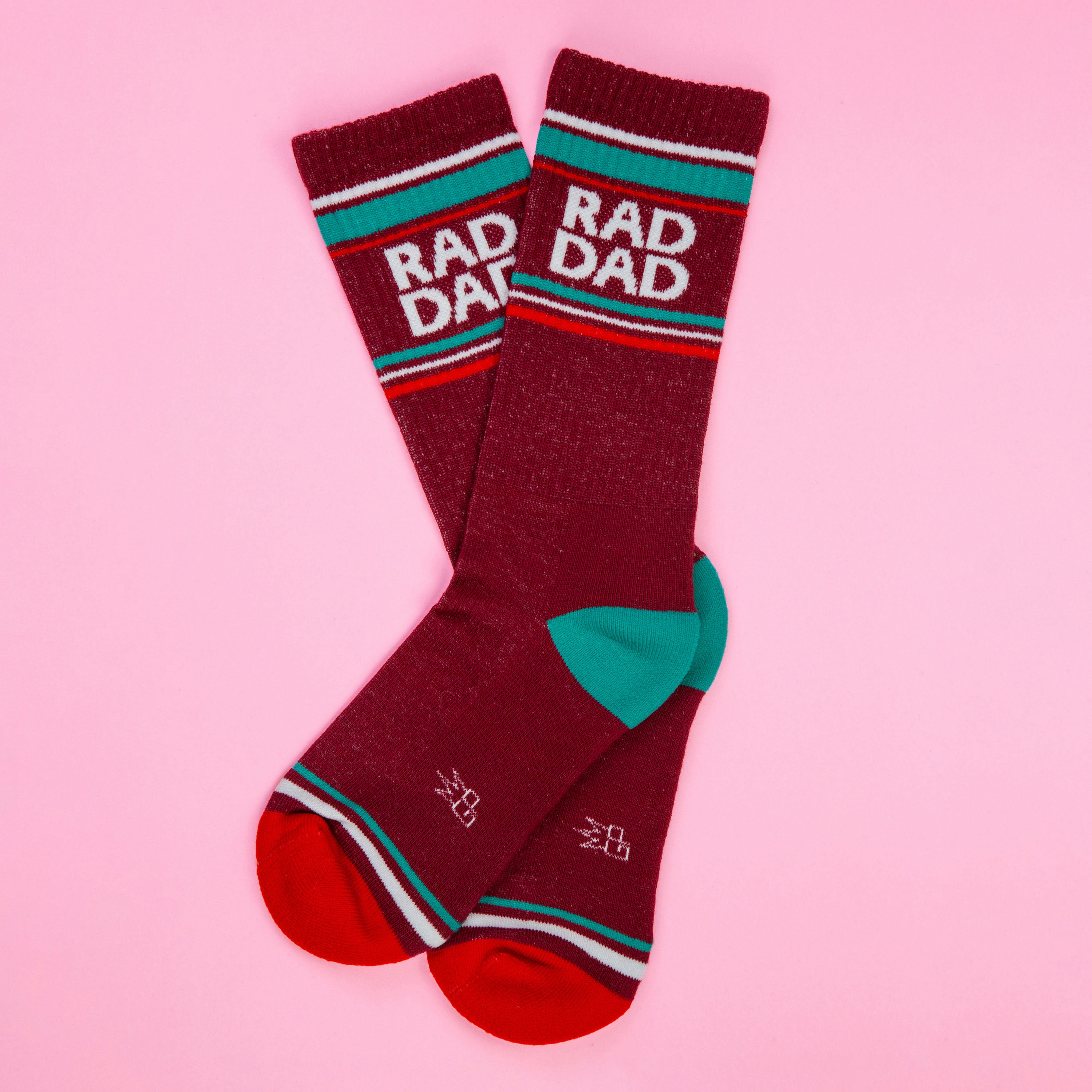 Flatlay image of two maroon Rad Dad socks on a pink background. [lf]
