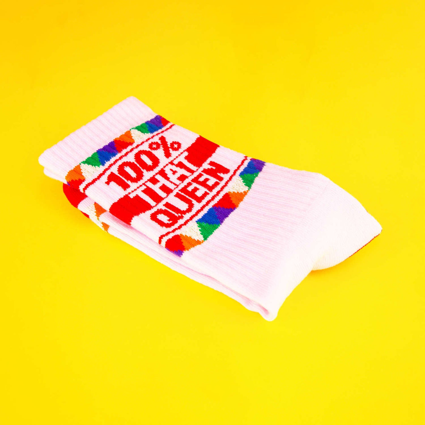 Close-up of the folded '100% That Queen' socks on a yellow background. [lf]