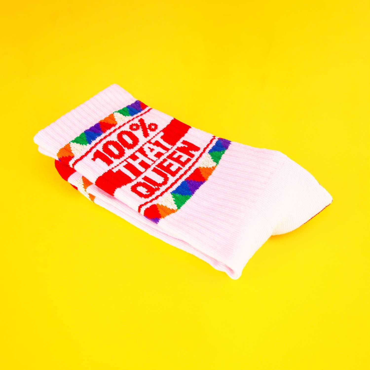 Close-up of the folded '100% That Queen' socks on a yellow background. [lf]