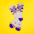 Pair of 'Proud Gay Dad' socks on a yellow background, displayed in an X shape. [lf]